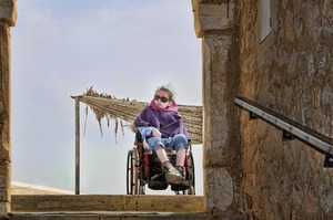 une enfant handicapée est avec son fauteuil en haut d'un escalier