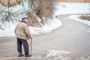 Un veil homme marche seul aidé d'une canne sur une route de campagne