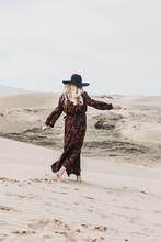 une femme marche sur la dune avec de un vêtement long et un chapeau